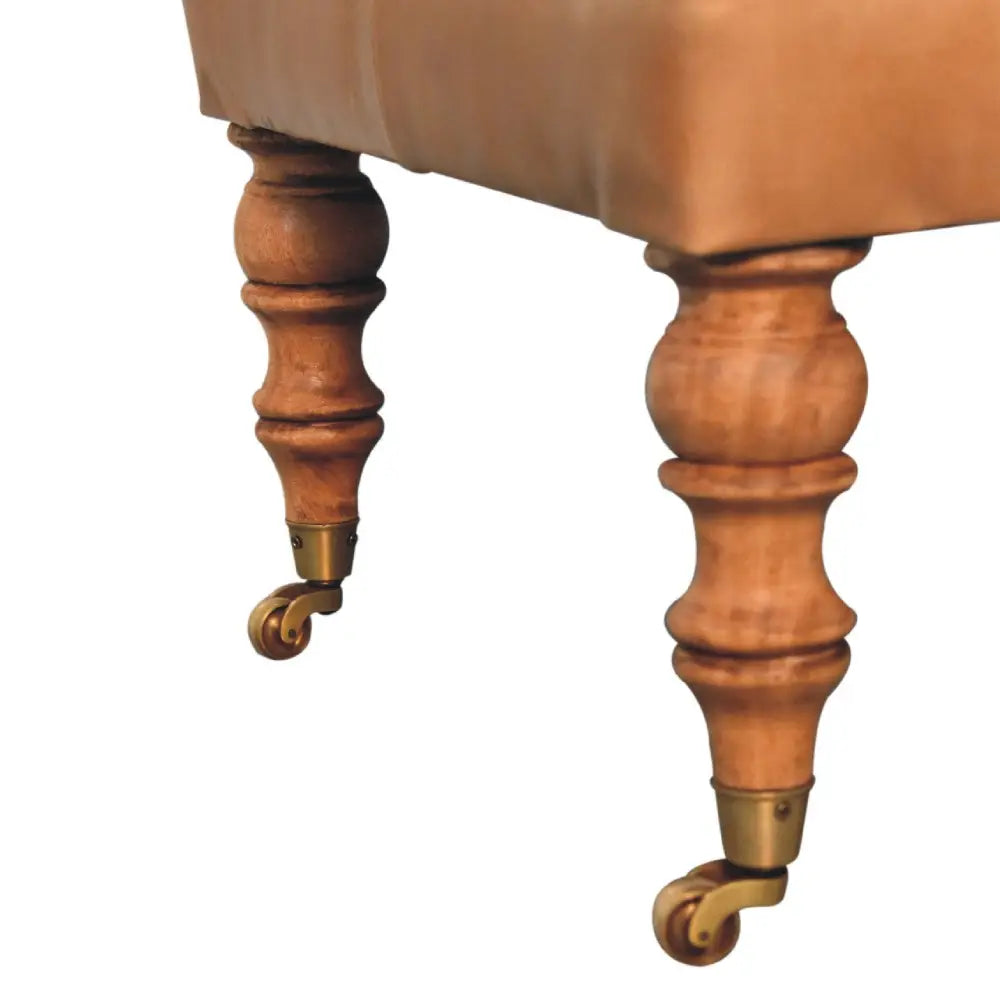 Tan buffalo leather ottoman with solid mango wood base, deep-buttoned top, and light walnut hand-turned feet. Leg view