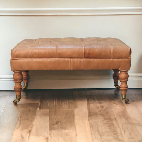 Tan buffalo leather ottoman with solid mango wood base, deep-buttoned top, and light walnut hand-turned feet. Full view in a living space